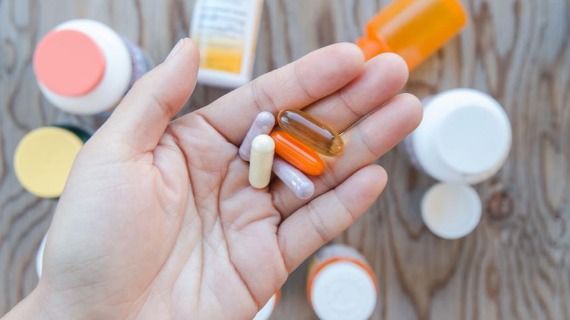 Person holding a collection of different-coloured pills and capsules in their hand
